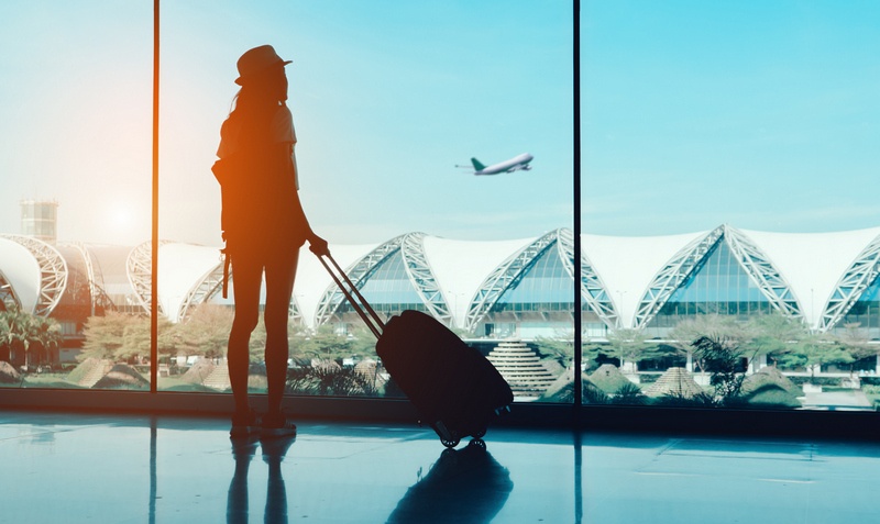 woman on a layover in the airport with suitcase watching a plane take off